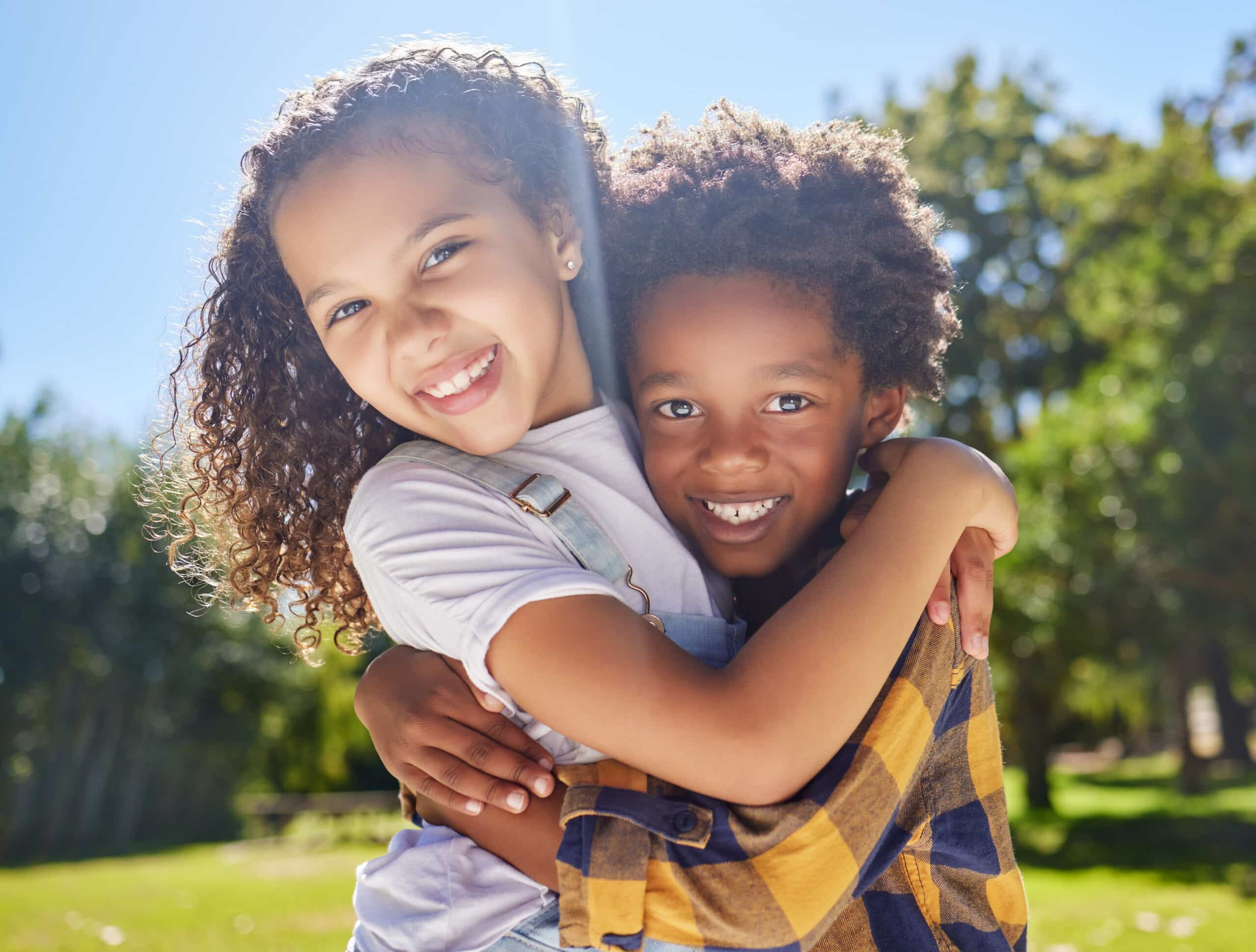 Portrait, kids and friends hugging in a park together for fun, bonding or playing in summer. Hug, children or diversity with girl and boy best friends embracing in a garden during the day AdobeStock 586528263 scaled